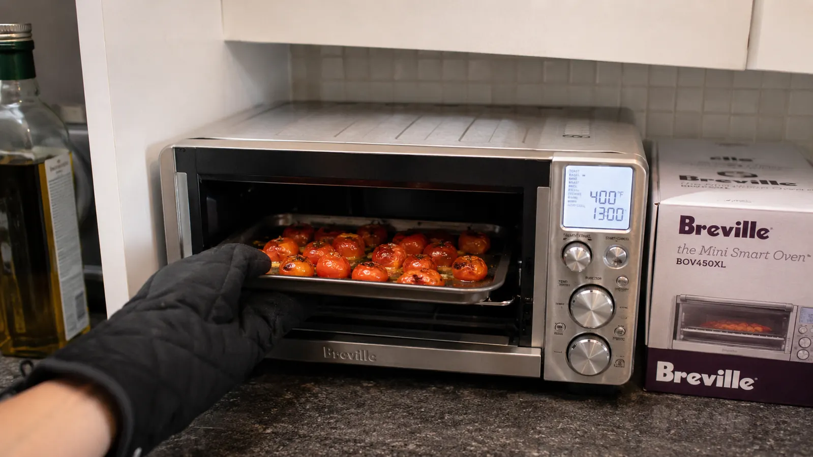 Hand sliding a small baking tray with roasted cherry tomatoes into the Breville BOV450XL on a tight kitchen counter