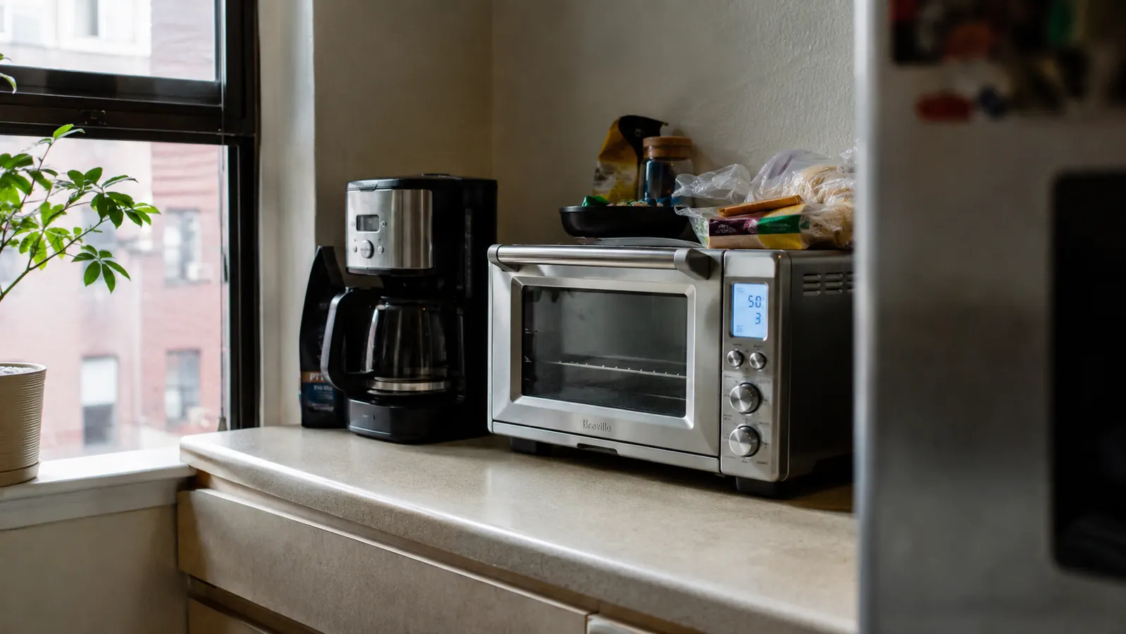 Breville BOV450XL Mini Smart Oven sitting on a narrow kitchen counter between a coffee maker and a spice rack in a small Dallas apartment