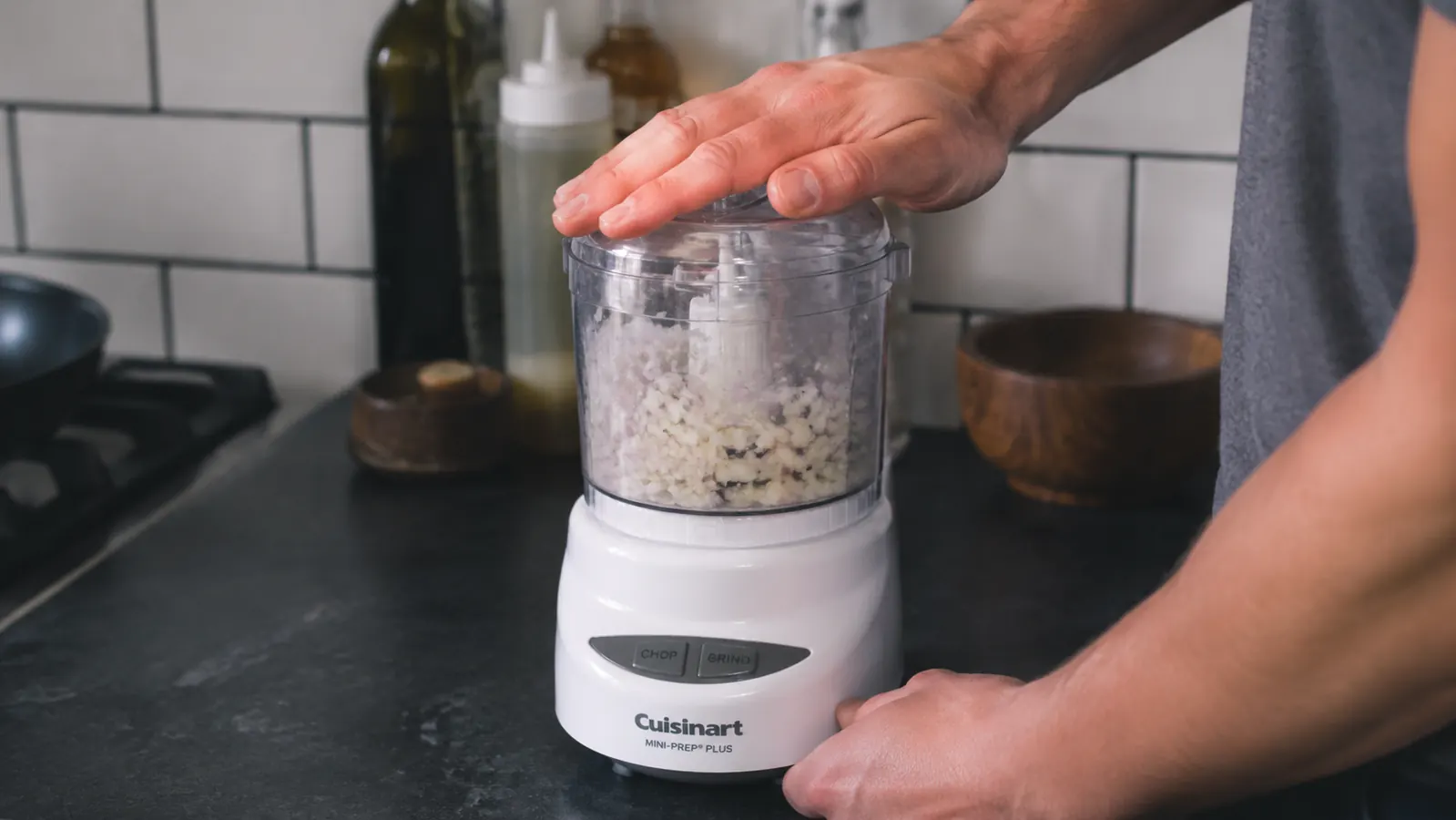 Hand pressing lid of Cuisinart Mini-Prep Plus to pulse a pile of onions and garlic in the 3-cup bowl