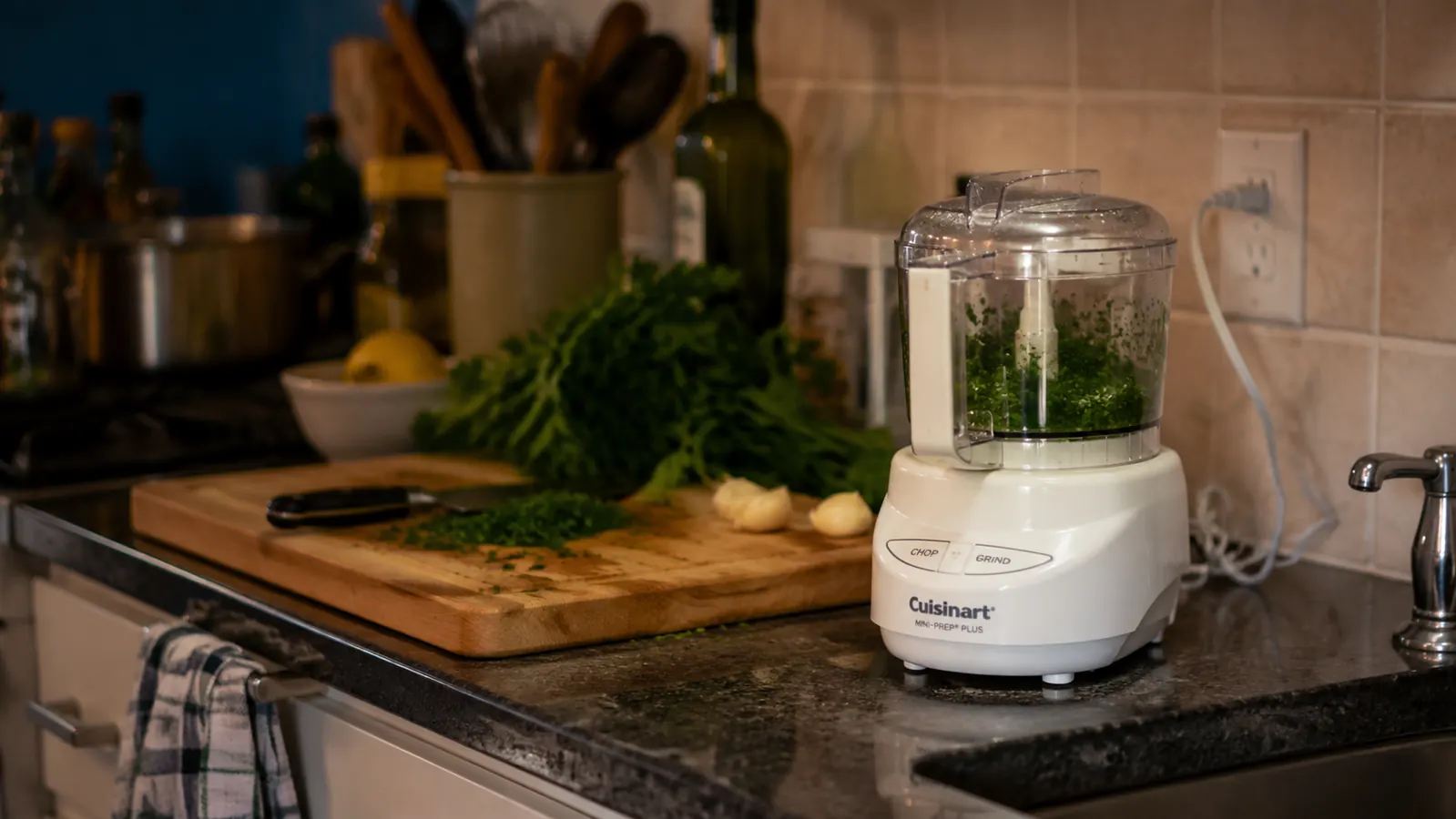 Cuisinart Mini-Prep Plus white food processor on a small apartment kitchen counter next to a cutting board with fresh herbs