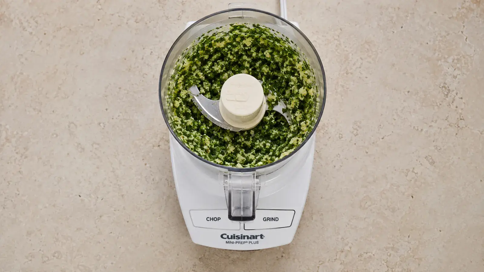 Minced garlic and fresh herbs in a small food processor bowl after processing, ready to scrape out